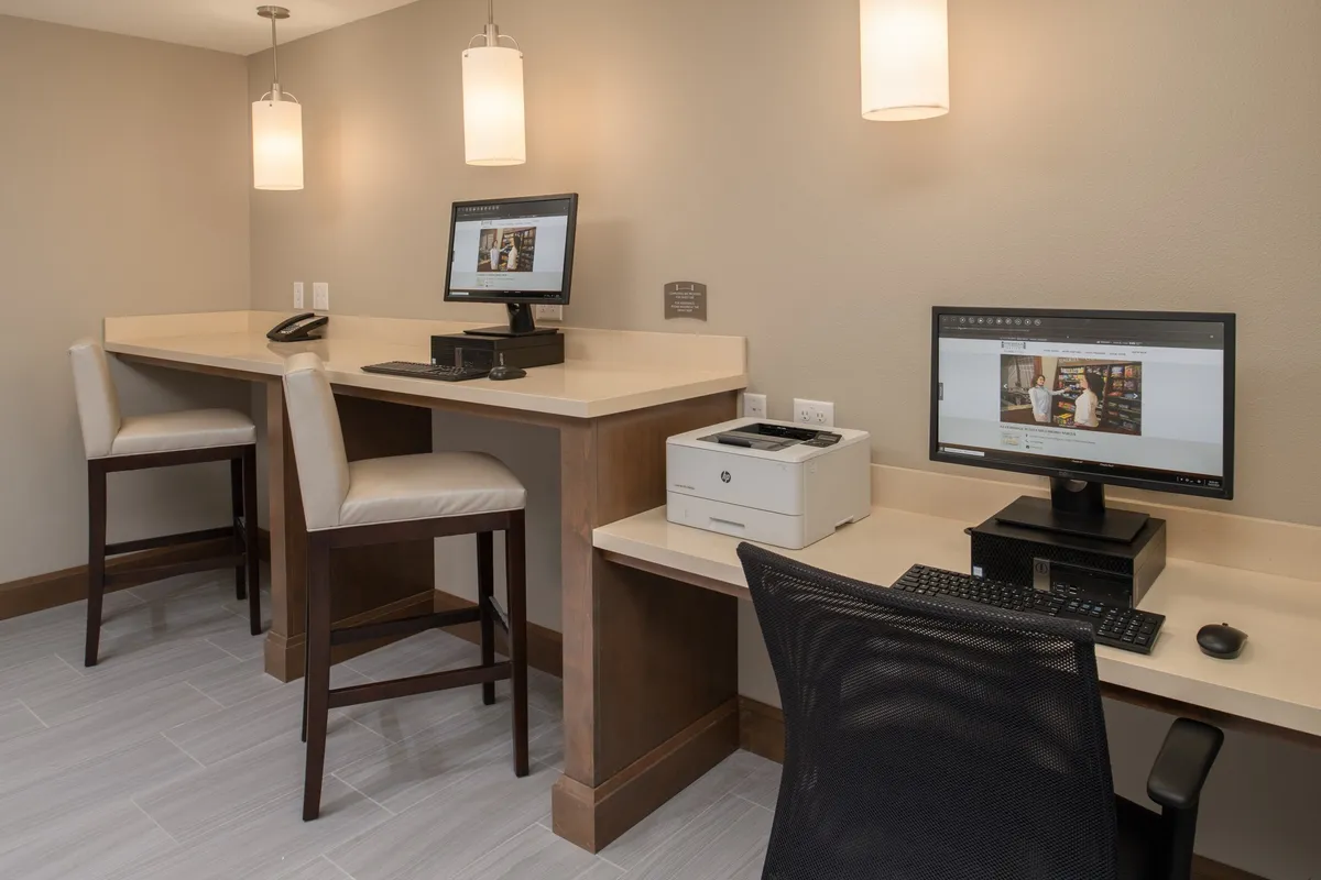 A modern interior workspace featuring computers, a printer, and bar-style seating, designed for focused work. The area is well-lit and organized, emphasizing productivity and access to high-speed Wi-Fi and office-like amenities.
