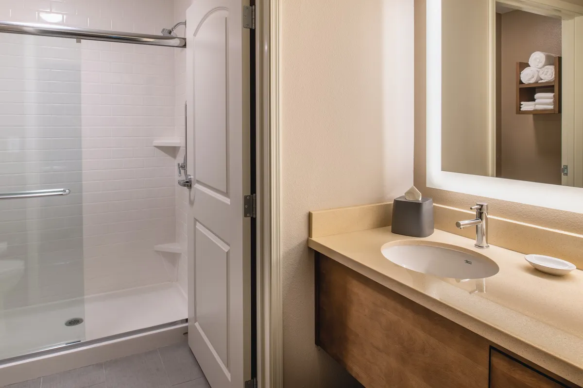 A modern, serene bathroom scene featuring a glass-enclosed shower, sleek sink and countertop, and a well-lit mirror. Fresh towels are neatly placed, and toiletries are arranged on the countertop, evoking a sense of luxury and personal care.